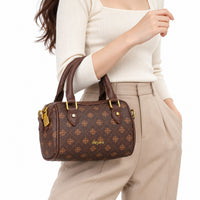 A woman wearing a cream ribbed sweater and beige trousers carries a small brown monogram handbag with gold-tone hardware and the brand name 'dejiwu' on the front, against a plain white background.