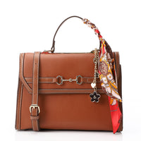 Brown leather handbag with a colorful scarf draped over the handle on a white background